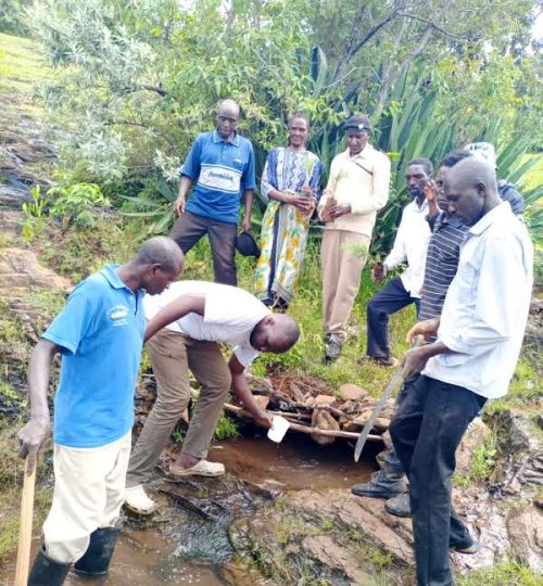 Image source: POTI | Community members taking a photo at Chepsolei Spring before planting the trees